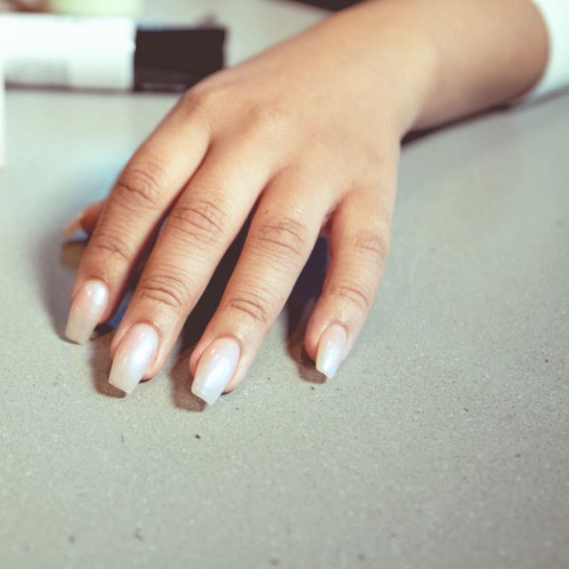Client's hand with a fresh pale manicure resting on a studio table