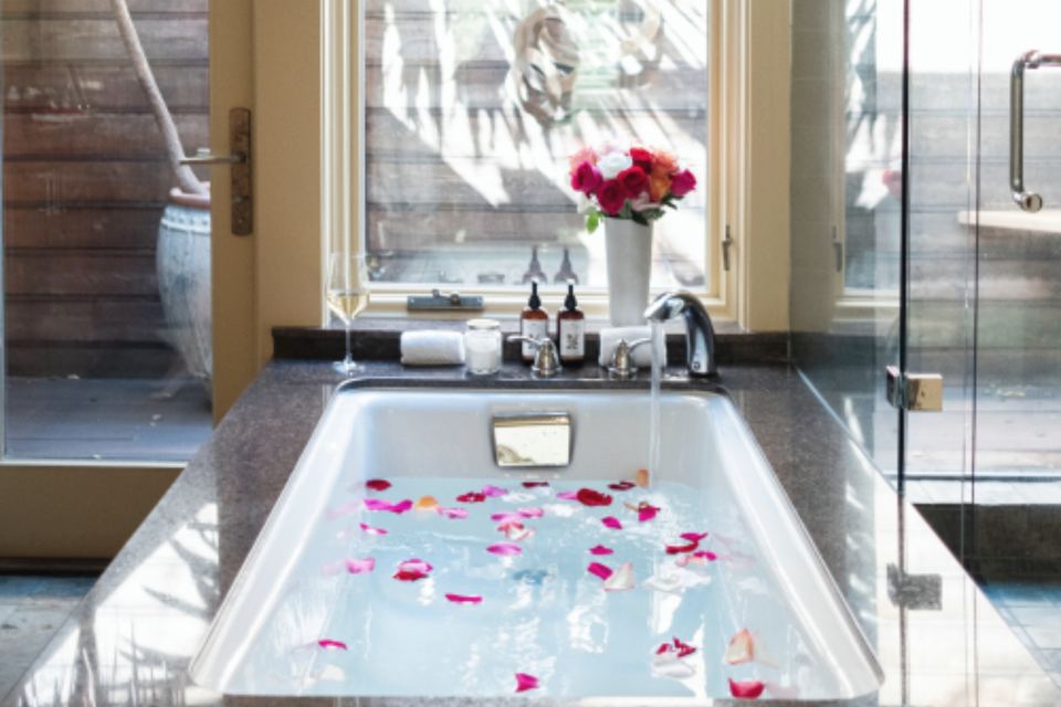 Calm spa bathroom with a rose petal bath, fresh flowers and a sunny window